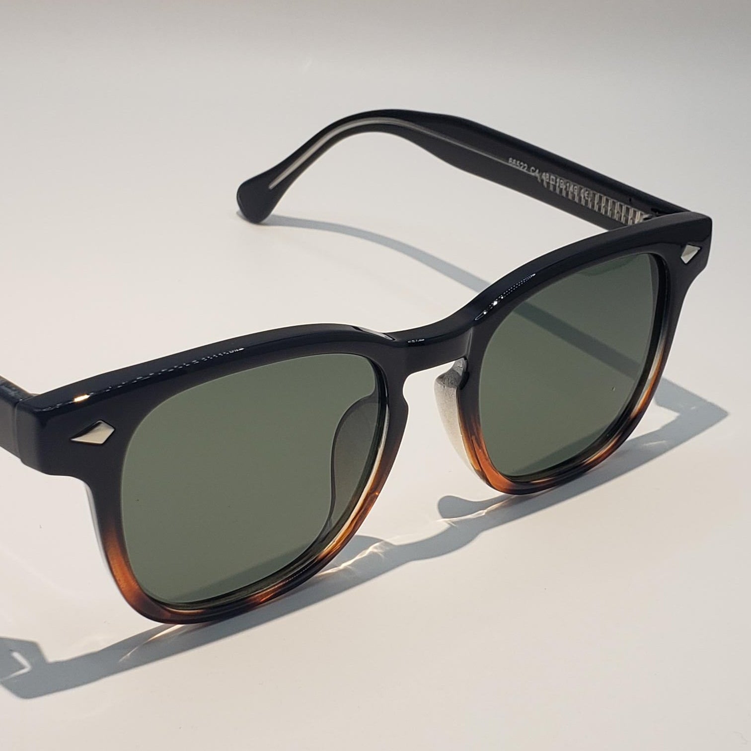 Sunglasses with tortoiseshell frame and green lenses on a light gray background