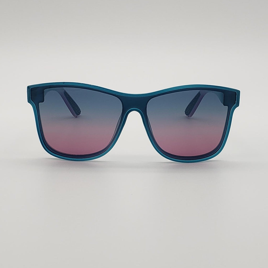 A pair of square sunglasses with a translucent teal-blue frame and gradient lenses that fade from dark blue at the top to pink at the bottom, shown on a neutral light gray background.