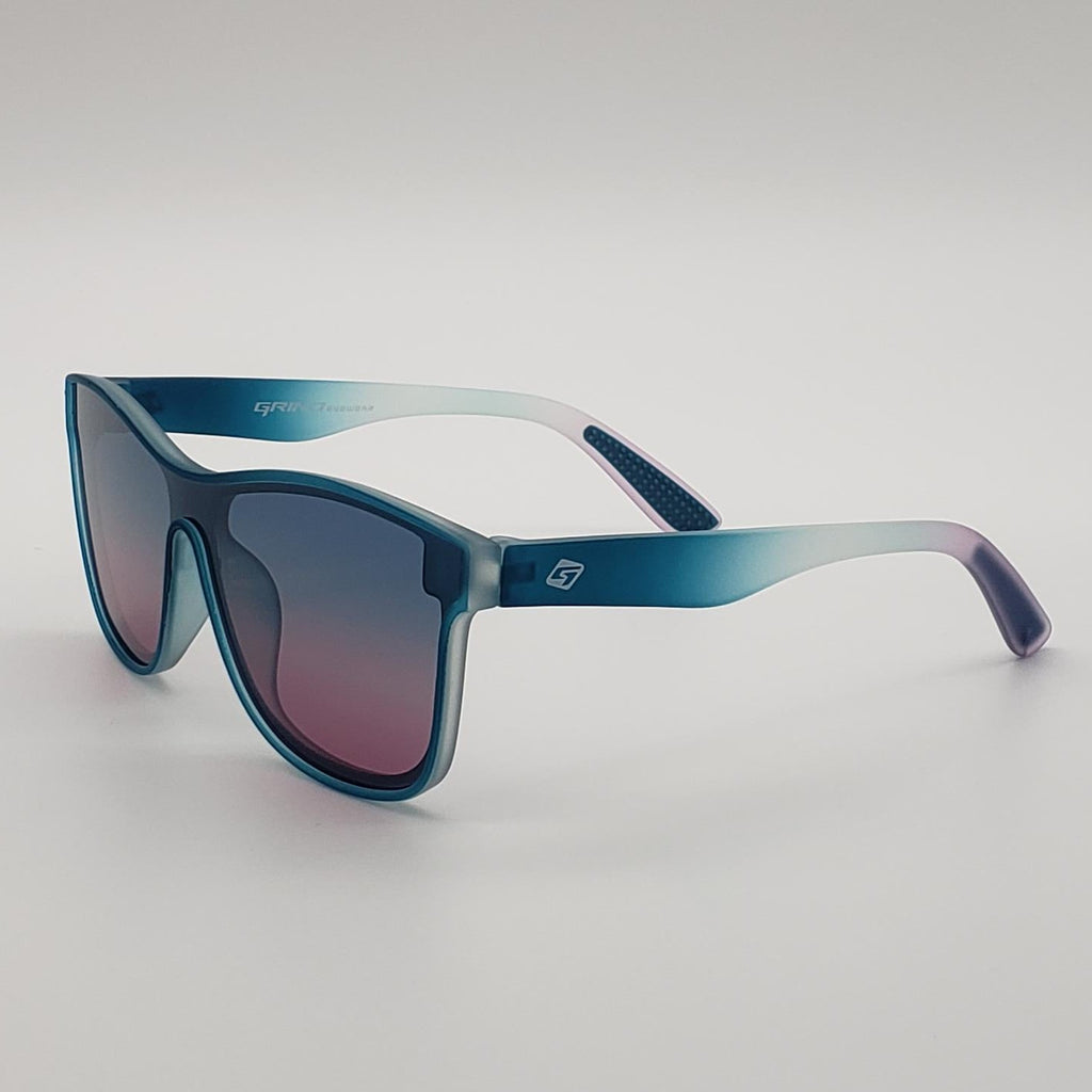 A pair of oversized sunglasses with a translucent blue-to-purple gradient frame and gradient lenses, shown on a neutral light gray background.