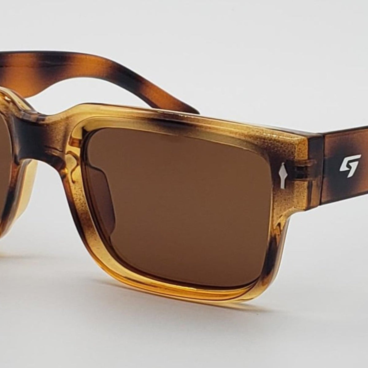 Square sunglasses with a translucent tortoiseshell frame in amber and brown tones, paired with dark brown lenses, shown on a light gray background.