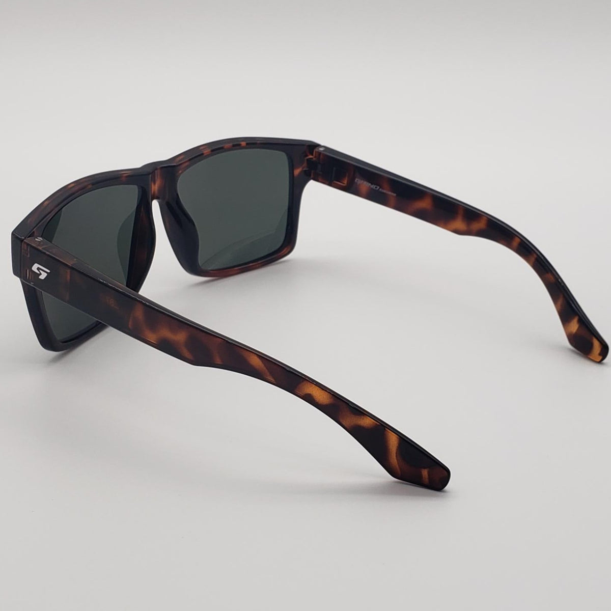 Tortoiseshell sunglasses with dark tinted lenses, shown from a three-quarters angle on a light gray background.