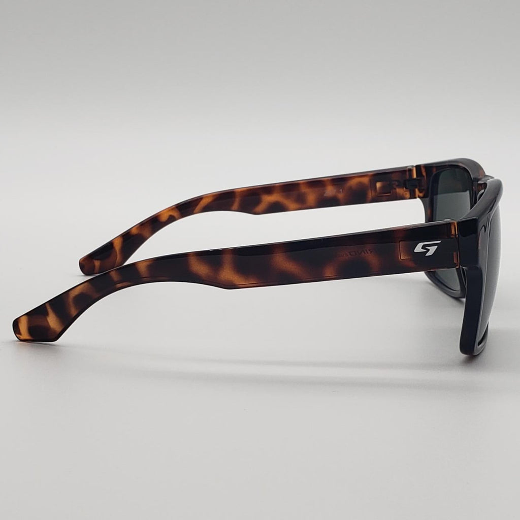A pair of square-frame sunglasses with a classic tortoiseshell pattern in brown and black, featuring dark lenses and a small white stylized 'G' logo on the temple arm, set against a neutral gray background.