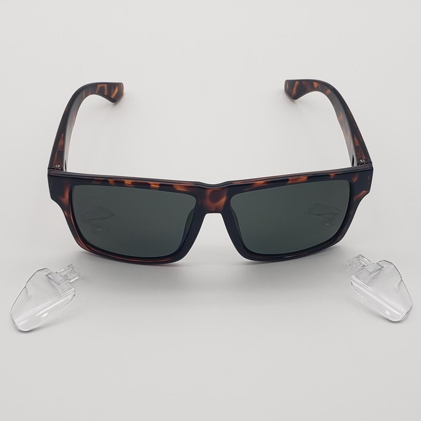 Square sunglasses with a dark brown and black tortoiseshell frame and dark gray lenses, displayed on a light gray background with two clear plastic nose pads below.