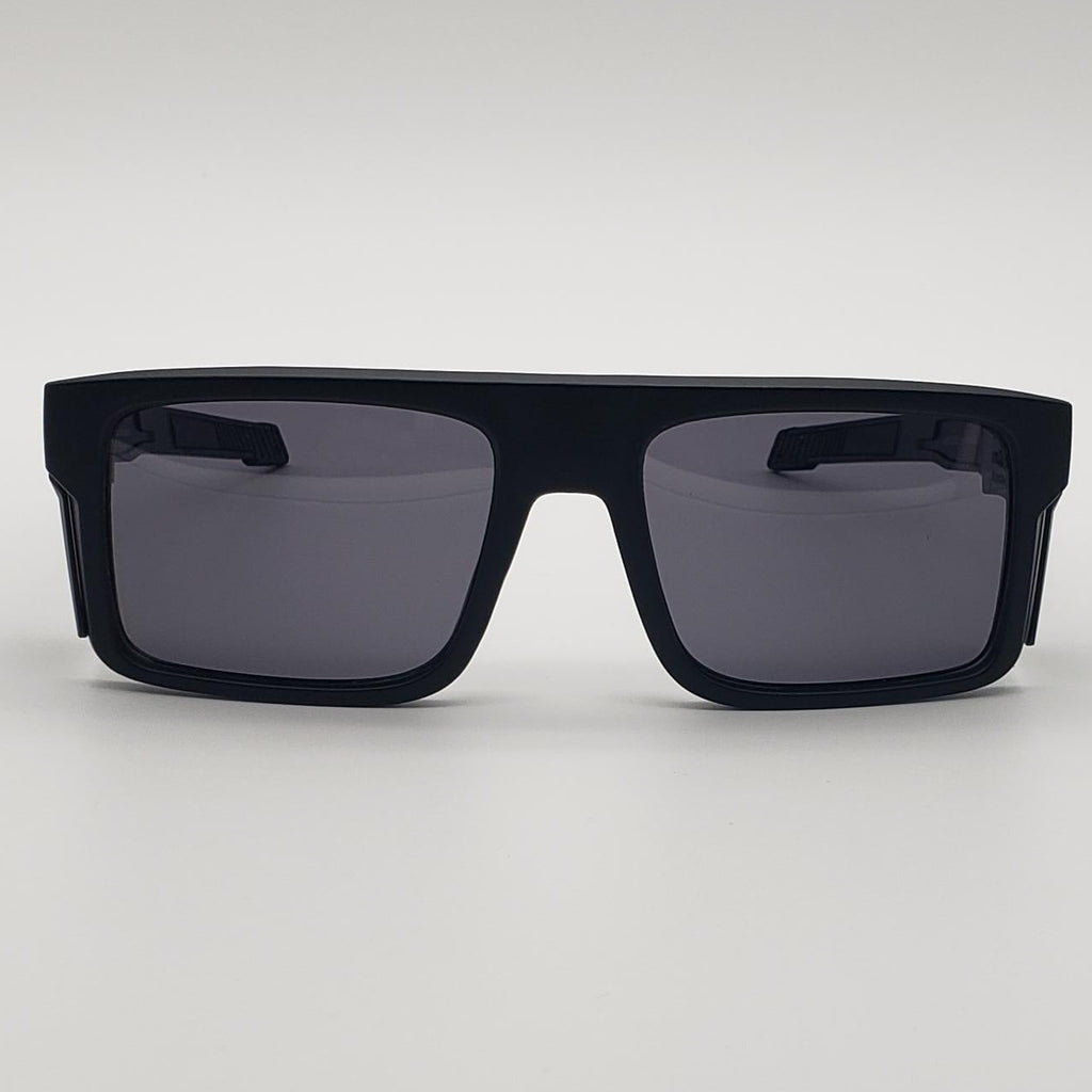 A pair of oversized square sunglasses with a matte black frame and dark gray lenses, photographed against a neutral light gray background.