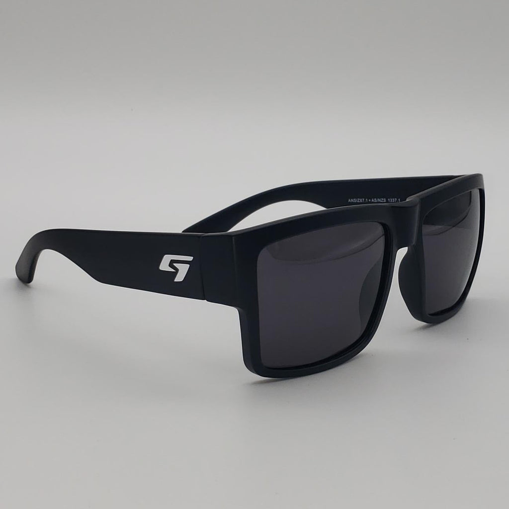 Black square-frame sunglasses with dark lenses and a white stylized 'S' logo on the temple, shown on a light gray studio background.
